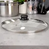 A glass pot lid with a black handle sits on a countertop. Podgląd zdjęcia produktu
