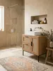 Der Badschrank mit Schubladen und Tür aus Rattan steht neben einer freistehenden Badewanne und schafft eine organisch-moderne Badezimmereinrichtung._#sku_SAFWL6.876# Produktbild-Vorschau