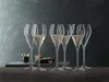 A set of six champagne flutes, some filled with champagne, arranged on a dark surface against a textured dark gray background. Produktbild-Vorschau