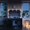 A vanity table with LED lights and a stool, set up in a room with windows showing a snowy mountain landscape at night. Náhled obrázku produktu