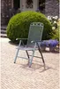 A gray folding chair sits on a brick patio in front of a large green bush and a house. Produktbild-Vorschau