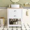 A white bathroom vanity with a ceramic sink and various toiletries displayed on the open shelf. Produktbild-Vorschau