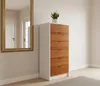 A tall, narrow dresser with white sides and wooden drawers stands in a room next to a gold-framed mirror. A potted snake plant sits on top of the dresser. Produktbild-Vorschau