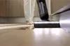A person is using a wet/dry vacuum cleaner to clean up a spill on a wooden floor. Náhled obrázku produktu