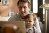A man is holding a baby and looking at a laptop. Anteprima dell’immagine prodotto