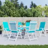 A white patio table and chairs with turquoise cushions are set up on a paved patio, surrounded by greenery and a wooden fence. Produktbild-Vorschau