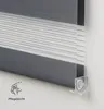 A close-up view of a gray and white striped roller blind, showing its texture and a small clear plastic bracket attached to the bottom edge. Voir les images du produit