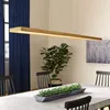 A dining room setting with a wooden LED pendant light over a table, chairs, and a plant. Náhled obrázku produktu
