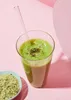 A glass of green smoothie with a straw and a small bowl of hemp seeds next to it, on a pink background. Produktbild-Vorschau