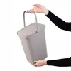 A person is holding a beige plastic trash can with a gray handle and lid. Produktbild-Vorschau