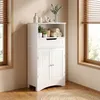 A white bathroom cabinet is shown in a corner next to a window, with blinds. Náhled obrázku produktu