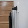 A close-up side view of a baby safety gate mounted on a wall next to a wooden staircase. Náhľad obrázku produktu