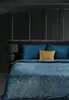 A bedroom scene with a bed covered in a blue blanket with a gold leaf pattern. Podgląd zdjęcia produktu