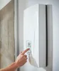 A hand is shown pressing a button on a white wall-mounted water heater. Produktbild-Vorschau