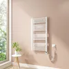 A white electric towel radiator mounted on a light pink wall next to a window. Produktbild-Vorschau