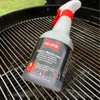 A bottle of grill cleaner is placed on a dirty grill grate. Produktbild-Vorschau