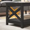 A close-up of a black coffee table with an X-shaped frame, showing storage space below. Orange arrows highlight a feature or area of interest. Produktbild-Vorschau