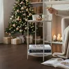 A cozy Christmas scene with a decorated tree, gifts, a fireplace, and a side table with mugs and books. Produktbild-Vorschau