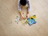 A child is playing with LEGOs on a wooden floor. Produktbild-Vorschau