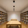 A long, well-lit room with bookshelves lining the walls and wooden tables in the center. Náhled obrázku produktu