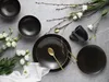 A flat lay of dark brown ceramic dinnerware with gold accents, accompanied by white flowers and branches. Produktbild-Vorschau