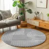 A circular rug with a geometric pattern is placed on a wooden floor in a living room, next to a gray sofa and a wooden cabinet. Voir les images du produit