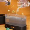 A hand is adding essential oil to an aroma diffuser filled with water, with bubbles containing small green bears and white flowers floating around. Voir les images du produit