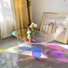 A modern, iridescent acrylic coffee table with a vase of flowers on it, placed in a well-lit room with curtains and a painting in the background. Light refracts through the table, casting colorful patterns on the floor. Anteprima dell’immagine prodotto