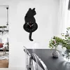 A black cat-shaped wall clock is mounted on a white wall above a dining table with transparent chairs. Produktbild-Vorschau