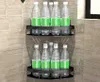 Two black corner shelves are mounted on a tiled wall, each holding several clear plastic bottles with green labels. Náhľad obrázku produktu