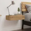 A bedside table with a lamp, books, and a plant next to a bed. Produktbild-Vorschau