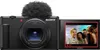 A Sony ZV-1 II digital camera with a microphone attachment is shown with its screen displaying a group of people. Produktbild-Vorschau