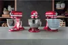 Three red stand mixers with different bowls are displayed on a countertop in front of a kitchen shelf. Voir les images du produit
