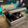 A bedroom scene with a bed that has its storage compartment open, revealing various items inside. A computer desk with a monitor is visible in the background. Náhled obrázku produktu