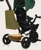 A close-up view of a green and black children's tricycle, with a green storage bag attached and a brown basket with toys at the bottom. Produktbild-Vorschau