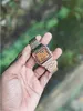 A hand holding a gold digital watch with a blurred green and brown background. Produktbild-Vorschau