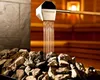 Water being poured from a ladle onto hot sauna rocks. Produktbild-Vorschau
