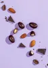 A top-down view of chocolate-covered almonds and pieces of dark chocolate scattered on a light purple background. Produktbild-Vorschau