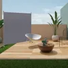 An outdoor patio scene with a grey privacy screen, a white chair, and a coffee table with decorative items. Anteprima dell’immagine prodotto
