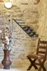 A wine rack mounted on a stone wall, with a vase of flowers and a wooden chair. Podgląd zdjęcia produktu