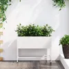 A white raised garden bed filled with green plants and white flowers sits on a wooden deck against a white wall. Green vines hang from above. Produktbild-Vorschau