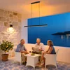 Three people are sitting on a patio at dusk, with a view of the sea and distant lights. Produktbild-Vorschau