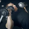 A man is lying on a bench and lifting dumbbells. Produktbild-Vorschau