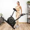 A woman stands next to a stationary bike in a home gym setting. Náhľad obrázku produktu