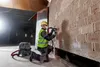 A construction worker is using a power tool with a vacuum attachment to drill into a brick wall. Produktbild-Vorschau