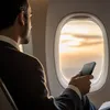 A man in a suit holding a power bank while looking out an airplane window at sunset. Produktbild-Vorschau