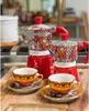 Two decorative coffee makers and two matching cups and saucers are arranged on a wooden surface, with a hint of a kitchen counter in the background. Produktbild-Vorschau