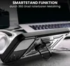 A black phone case with a silver ring stand is shown on a wooden surface, with a laptop and headphones in the background. Produktbild-Vorschau