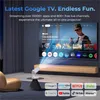 A projector is shown projecting an image onto a large screen in a living room setting. The screen displays the Google TV interface with various app icons and a movie poster. Several app logos are displayed at the bottom of the image. Produktbild-Vorschau