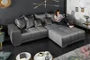 A woman is sitting on a large sectional sofa, reading a book. The sofa is in a modern living room setting with dark walls and a marble accent wall. Produktbild-Vorschau